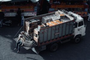 A truck loaded with crates of oranges parked at an urban market scene during daytime.